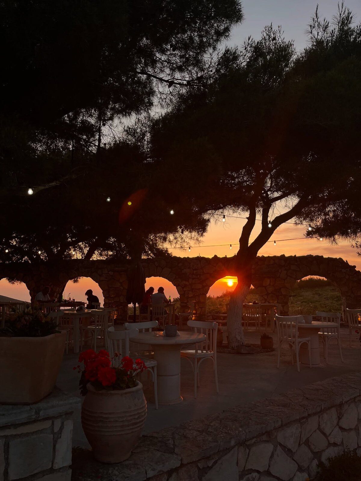Guests toasting wine glasses under a stone archway at sunset